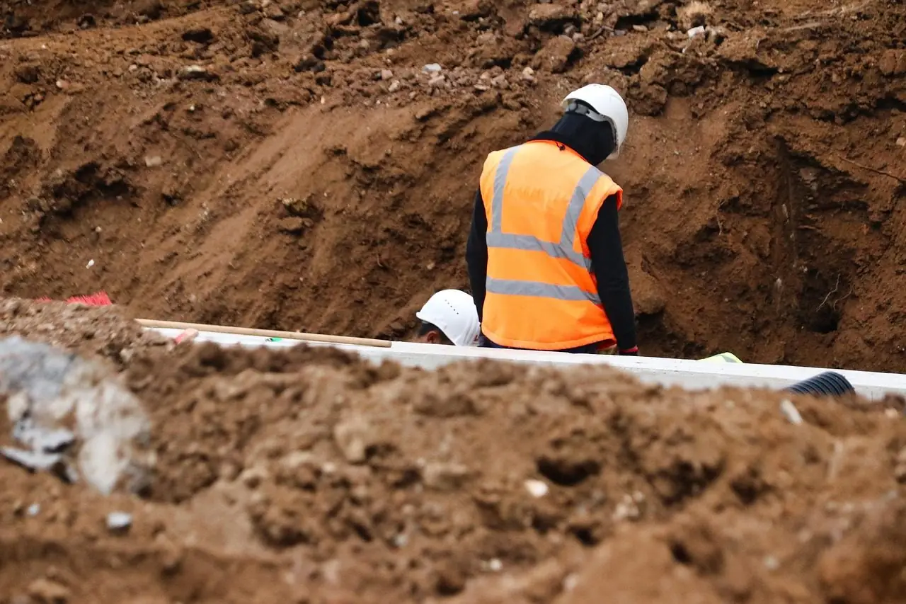 Worker in a hard hat and safety vest standing in an open dirt trench